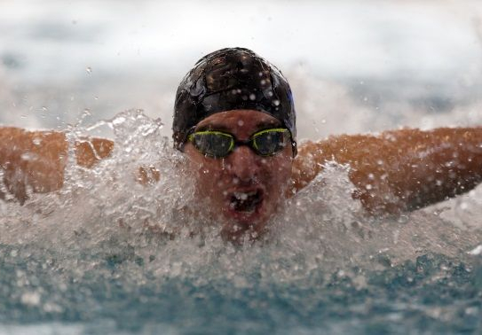Swimmer in cap and goggles performing butterfly stroke through splashing water