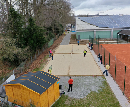 Personen spielen Boule auf Sandbahnen neben Tennisplatz