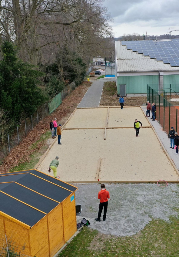 Personen spielen Boule auf Sandbahnen neben Tennisplatz
