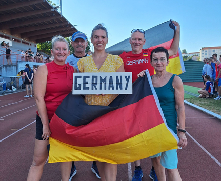 Fünf Athleten halten deutsche Fahne und Schild GERMANY auf Laufbahn