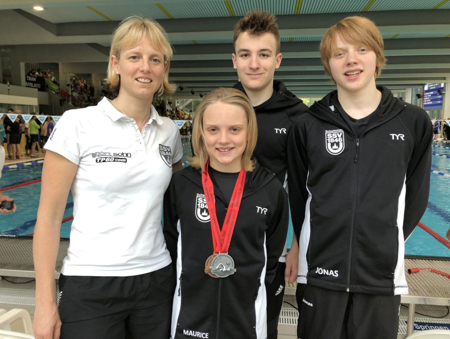 Vier Personen in Vereinsjacken am Schwimmbecken, Mädchen mit Medaillen