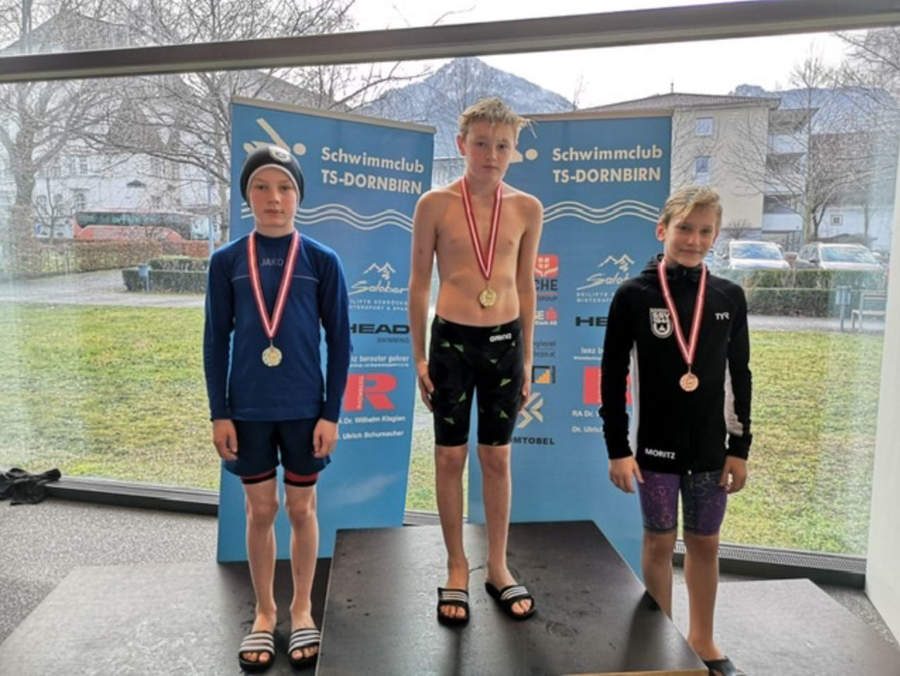 Drei jugendliche Schwimmer auf Siegertreppchen mit Medaillen Banner Schwimmclub TS-DORNBIRN