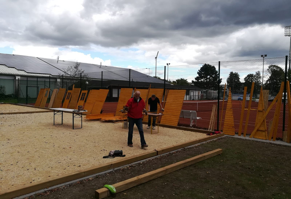 Zwei Männer montieren Holzpaneele an einem eingezäunten Sportplatz