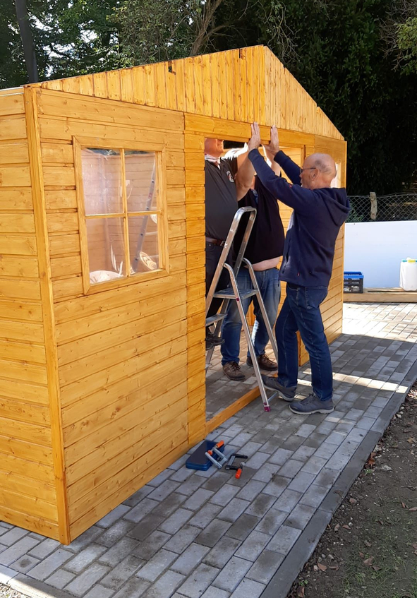 Drei Männer setzen Türrahmen an hölzernem Gartenhaus ein