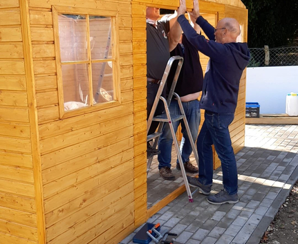 Drei Männer setzen Türrahmen an hölzernem Gartenhaus ein