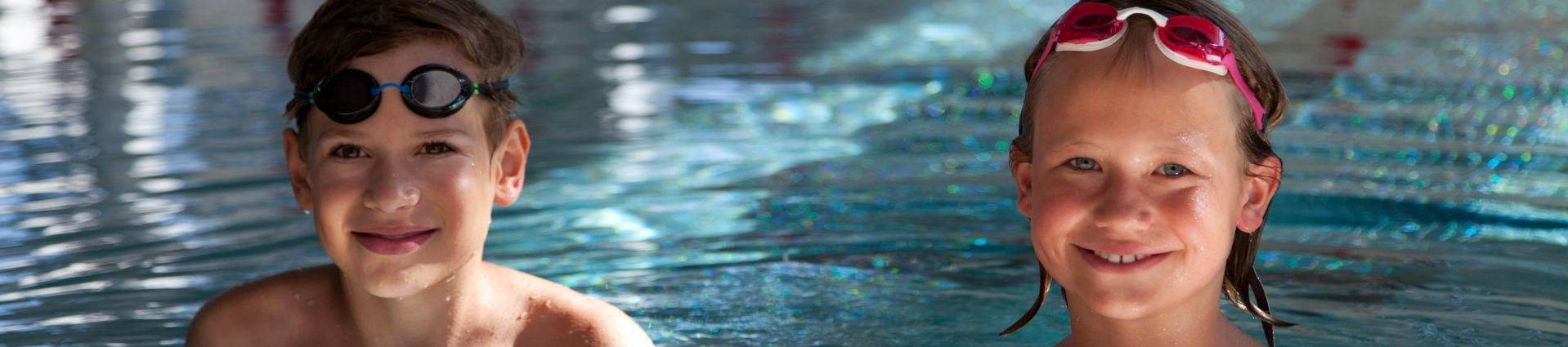Zwei Kinder mit Schwimmbrillen am Beckenrand im Schwimmbad
