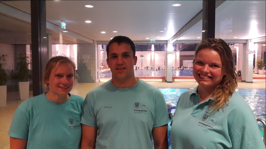 Drei SwimStars-Instruktoren in türkis T-Shirts vor Schwimmbecken
