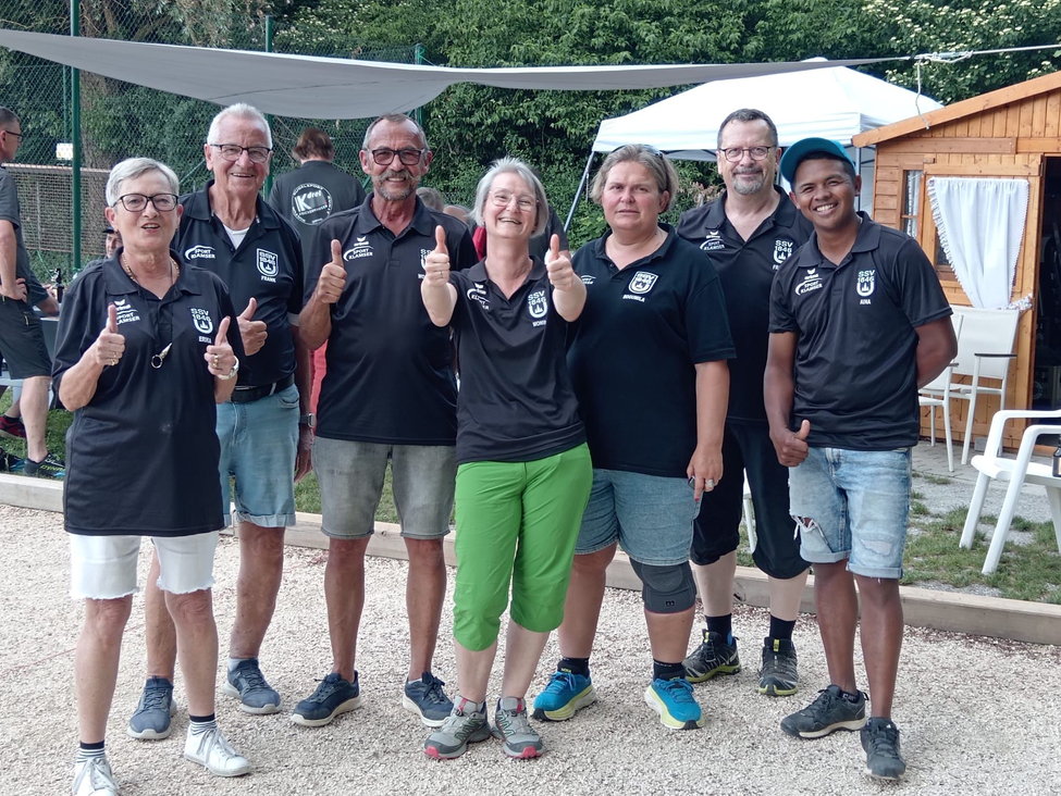 Eight team members in black shirts giving thumbs up outdoors