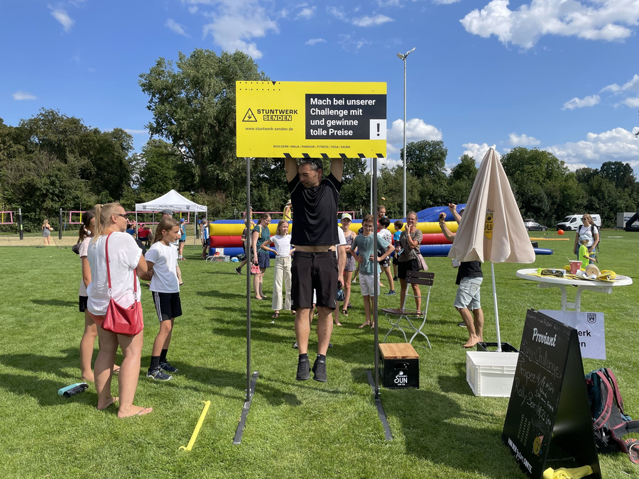 Mann hängt an Stange unter Schild Mach bei unserer Challenge mit
