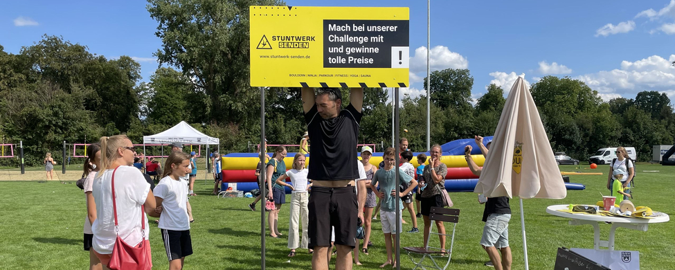 Mann hängt an Stange unter Schild Mach bei unserer Challenge mit