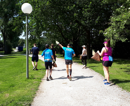 Läuferinnen und Läufer der Plogging Aktion auf dem Weg in die Au Plogging Gruppe joggt auf Parkweg mit Handschuhen und Müllsäcken