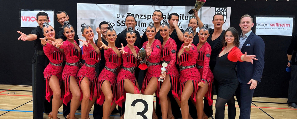 Formations-Team in roten Kostümen posiert mit Schild 3