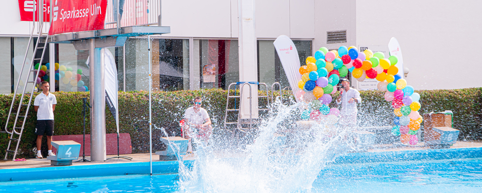 Ein Teilnehmer beim 1. Ulmer Arschbomben-Contest powered by Sparkasse Ulm springt vom 3-m-Turm und man sieht auf dem Bild den Moment, wo er ins Wasser eintaucht und seine Arschbombe eine ordentliche Wasserfontäne erzeugt.