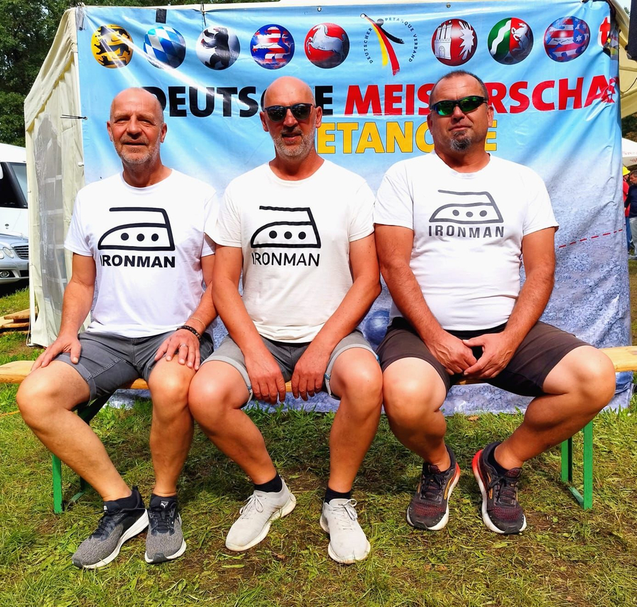 Drei Männer auf Bank in Ironman T-Shirts vor Deutsche Meisterschaft Petanque