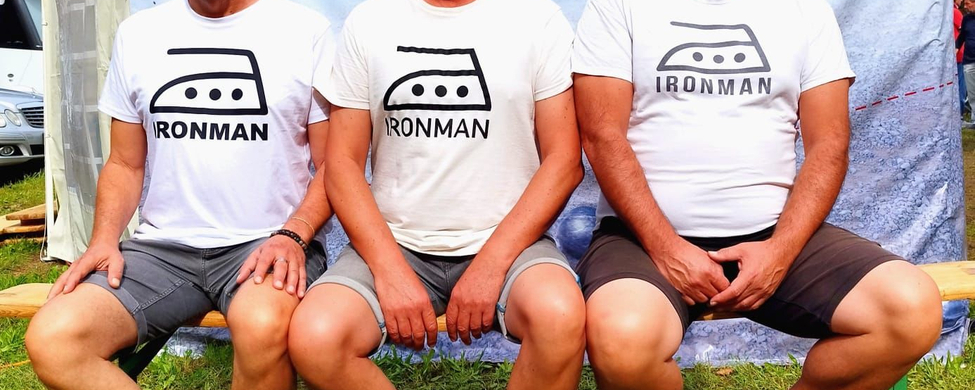 Drei Männer auf Bank in Ironman T-Shirts vor Deutsche Meisterschaft Petanque
