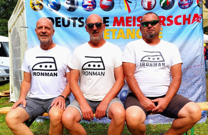 Drei Männer auf Bank in Ironman T-Shirts vor Deutsche Meisterschaft Petanque