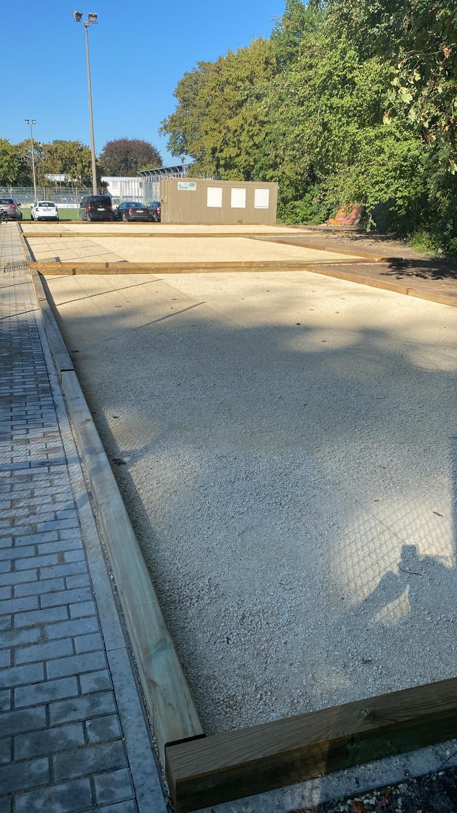 Gravel playing courts with wooden borders next to paved walkway