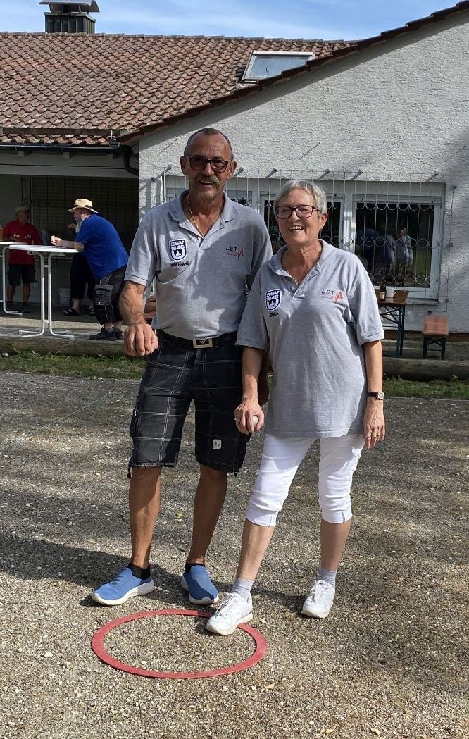 Zwei Personen in grauen Poloshirts stehen auf Kies neben einem roten Ring