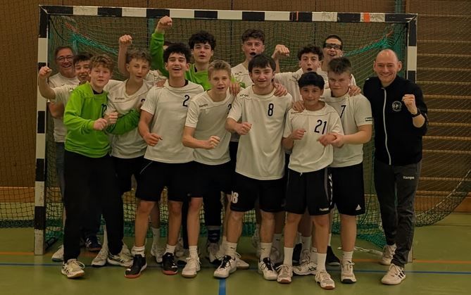 Männliche B-Jugend jubelnd vor Handballtor mit Trainern